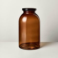 a brown glass bottle sitting on top of a white table next to a black lid