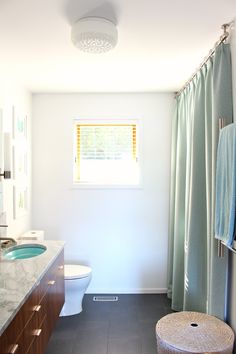 a bathroom with a toilet, sink and shower curtain in it's window area