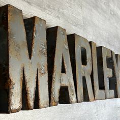 the word march written in rusty metal letters on a white wall with wood planks