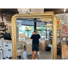 a man taking a photo in front of a large gold framed mirror at a furniture store