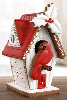 a red bird perched on top of a white birdhouse with holly and snowflakes