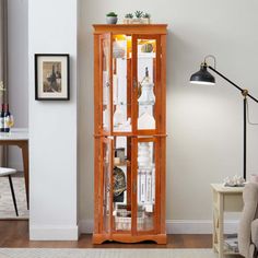 a tall wooden cabinet with glass doors in a living room next to a table and chair