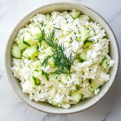 a white bowl filled with cucumbers and dill sprinkled on top