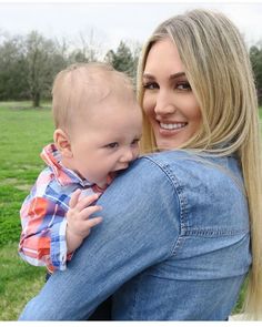 a woman is holding a baby in her lap and smiling at the camera, with grass behind her