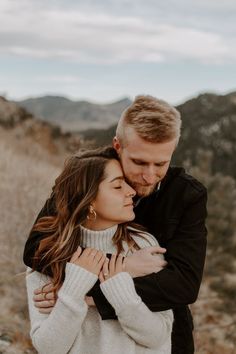 a man and woman embracing each other in the desert with mountains in the back ground