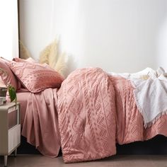 a bed with pink comforter and pillows on it next to a nightstand in a bedroom