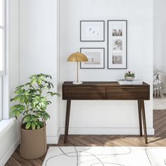 a white room with a wooden desk and two framed pictures on the wall next to a potted plant