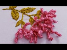 two crocheted flowers are sitting on a piece of white fabric with yellow and pink thread