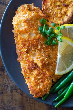 a blue plate topped with chicken, green beans and lemon wedges next to a slice of bread