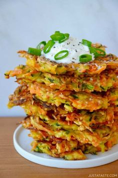 a stack of vegetable fritters on a plate with sour cream and green onions