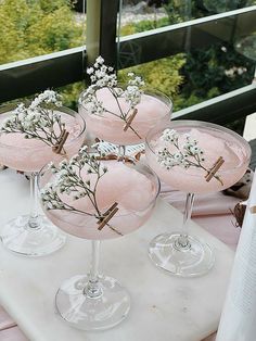 four martini glasses with flowers in them sitting on a white counter top next to a window