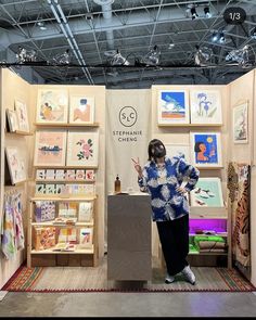 a woman standing in front of a booth with paintings on it's walls and wearing a face mask