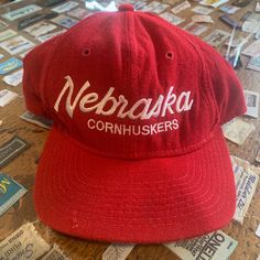 This is a vintage wool Nebraska Cornhuskers script hat from the 1990's, made by Sports Specialties. This hat is in good vintage condition with light wear and some faint yellowing on the band, there is one small moth hole which is pictured. Please also assess the photos carefully using your own personal judgement on the condition of the item.  Please see our FAQ's for more info on our cleaning and shipping policies.  **Hat will be shipped in a box** Retro Snapback Hat For Fan Gear, Retro Snapback Hat For Fans, Retro Cap For Game Day, Retro Fitted Cap For Fan Gear, Retro Game Day Cap, Vintage Red Six-panel Baseball Cap, Vintage Flat Brim Trucker Hat For Baseball Season, Vintage Snapback Fitted Hat, Vintage Trucker Hat With Flat Bill For Baseball Season