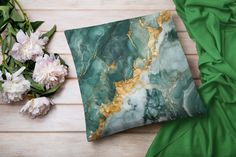 a green and gold marble pillow sitting on top of a wooden floor next to flowers