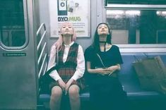 two women sitting on a subway train looking up at something in the air with their eyes closed