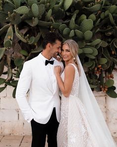 a bride and groom standing next to each other in front of a cactus wall at their wedding