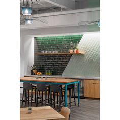 an industrial style kitchen and dining area with green brick wall behind the counter, along with wooden tables and chairs