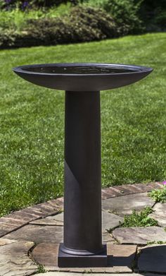 a black bird bath sitting on top of a stone slab in the grass next to a brick walkway