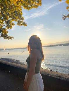 a woman is standing by the water at sunset