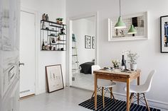 a dining room table with two white chairs and pictures on the wall above it, in front of a doorway