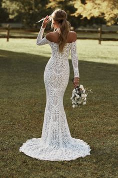 a woman in a white wedding dress standing on the grass with her back to the camera