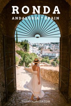 a woman in a white dress and hat walking through an archway with the words ronda andal spain