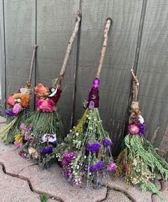 three brooms are lined up with flowers and twigs on them, against a wooden fence