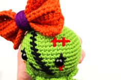 a crocheted green and orange stuffed animal with a bow on it's head