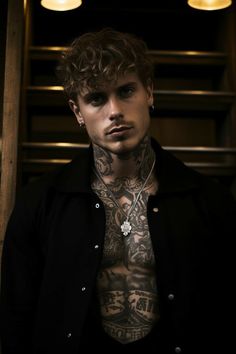 a man with tattoos on his chest standing in front of some stairs and lighting fixtures