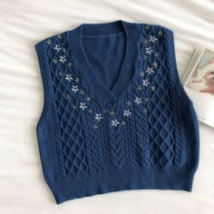 a blue sweater with flowers on it next to a book