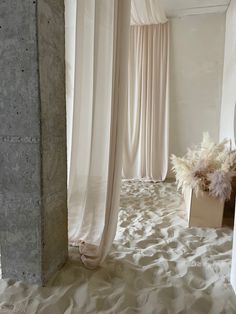 an empty room with white curtains and a plant in the corner on top of sand