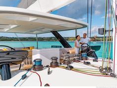 two men standing on the deck of a sailboat in the open water, talking