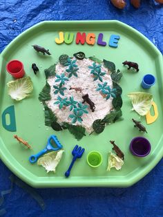 a green tray topped with lots of toys and writing on top of blue table cloth