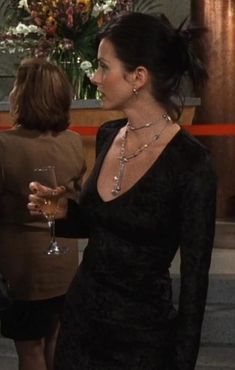 a woman in a black dress is holding a wine glass and talking to another woman