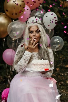 a woman in a white dress blowing out confetti on her birthday cake while surrounded by balloons and streamers