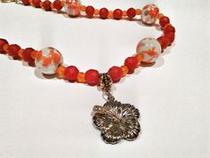 Red and Orange Hibiscus Beaded Necklace - Orange and Red Golden Flower Necklace - Ceramic Orange Statement Necklace Handmade vivid beaded necklace made of red and orange glass beads as well as round white cermaic beads with orange and pale purple swirls. Red and orange beads are faceted in a variety of size. There is a silver and gold hibiscus flower charm. The petals of the flower is silver and the center is gold. The center stem has 2 crystal like insets in it. Necklace is ended with a toggle clasp in gold tone and antique swirl design. Necklace Length from clasp to clasp: 19 1/2" Packaged and wrapped in a beautiful gift box. Perfect for yourself or as a gift. From a smoke-free and pet-free shop. Orange Beaded Necklaces With Lobster Clasp, Red Flower-shaped Beaded Necklaces For Gifts, Orange Flower Jewelry For Beach, Orange Flower-shaped Jewelry For Beach, Red Flower-shaped Beaded Necklace For Gift, Orange Flower-shaped Beach Jewelry, Red Faceted Beads Jewelry For Beach, Orange Flower Shaped Beaded Necklace For Gift, Red Flower-shaped Beads For Gifts