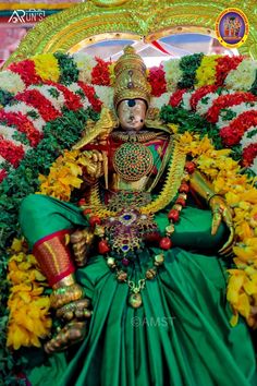 the statue is dressed in green and gold, with flowers around it's head