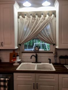 a kitchen sink under a window with curtains hanging from it's windowsills