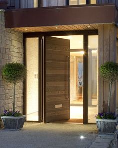 an entrance to a modern home at night with lights on the door and planters in front