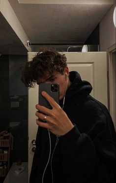 a young man taking a selfie in the mirror with his cell phone and headphones