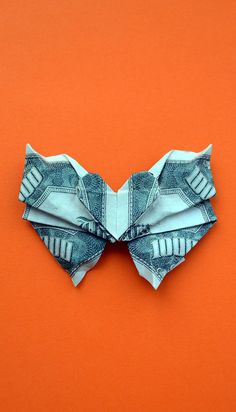 an origami bow made out of one hundred dollar bills on an orange background