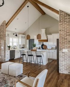 an open concept kitchen and living room with exposed brick walls, white cabinets, wood floors, and wooden beams