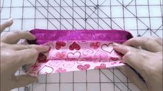 two hands are holding a pink bag with hearts on it and one hand is sewing the fabric