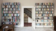 a living room filled with lots of books next to a stair case full of books