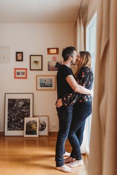 a man and woman standing next to each other in front of a window with pictures on the wall