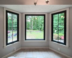 an empty room with three large windows and tile flooring in front of the window