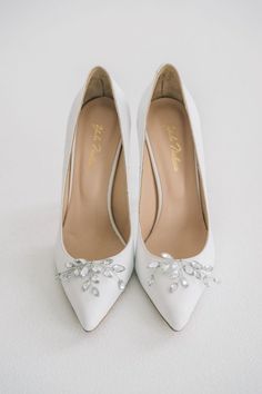 a pair of white wedding shoes with pearls on the toe and heels are shown in close up