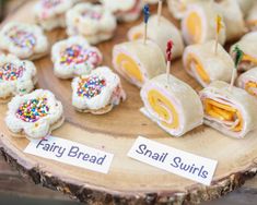 small sandwiches are arranged on a wooden plate with toothpicks stuck in them and labeled fairy bread