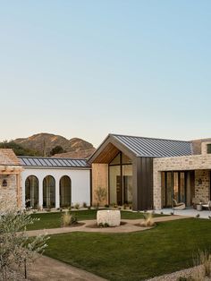 a modern house in the desert with grass and rocks on the front lawn, surrounded by mountains