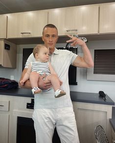 a man holding a baby in his arms while standing next to a kitchen counter top